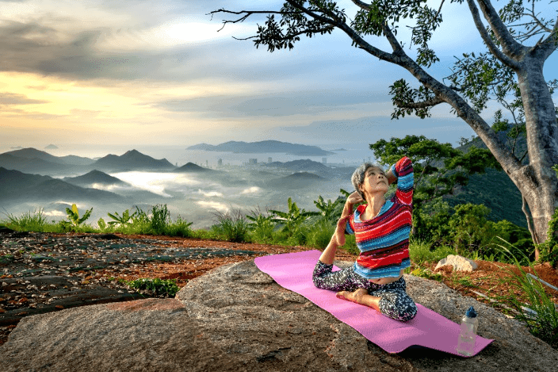 Woman sitting on a mountainous region, with mountain background, doing a yoga pose