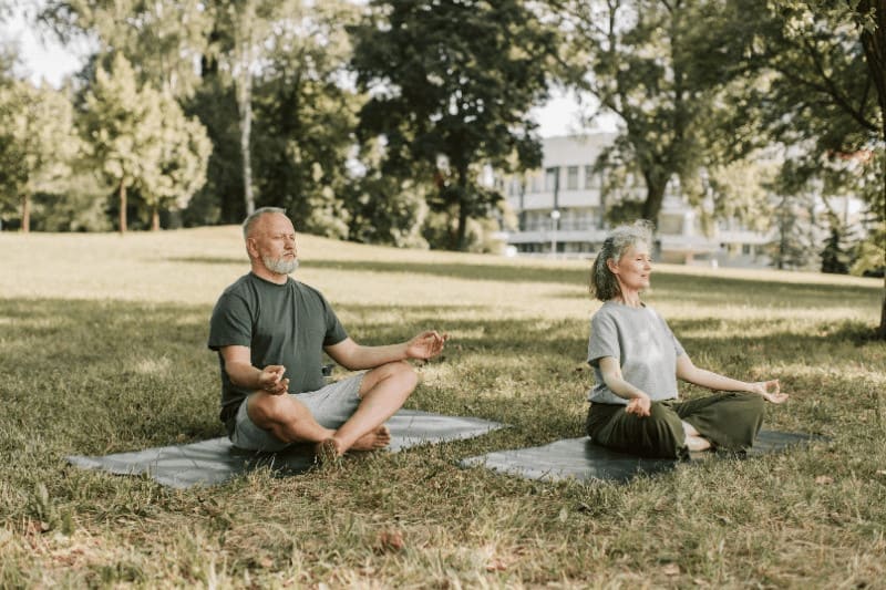 Couple sitting in the grass on their yoga mats, practicing breathing techniques